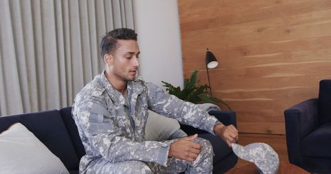 military soldier sitting on couch wearing full uniform and holding cap. captures a contemplative moment, reflecting personal lifestyle and patriotism. suitable for topics on military life, mental health, or veteran support. can be used in articles or advertisements related to armed forces or home life of soldiers.