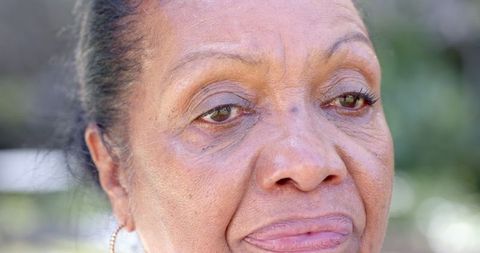 Senior Woman Gazing in Sunlit Garden with Gold Hoop Earring