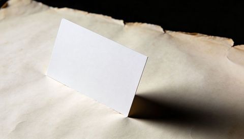 Blank white card standing on aged parchment casting dramatic long shadow for mockup
