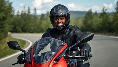 Smiling black rider cruising red sportbike on winding country road in leather gear