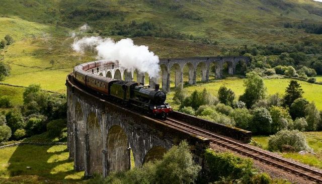 Vintage steam train crossing curved stone viaduct over highland valley with billowing steam