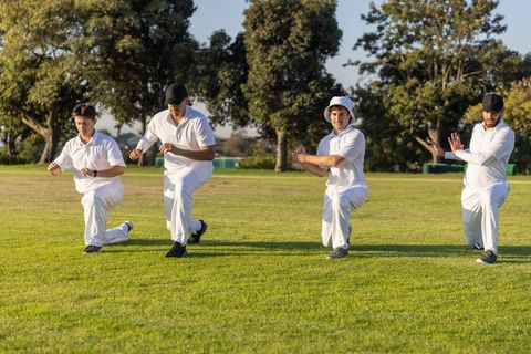 Four cricketers practicing catching drill on sunlit outfield