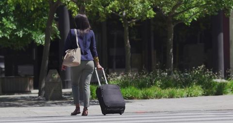 Businesswoman walking with suitcase across city street