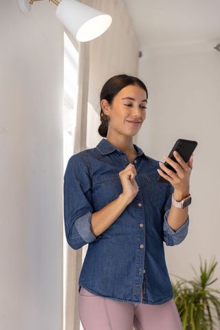 White woman tapping smartphone wearing smartwatch, smiling casual home wellness lifestyle
