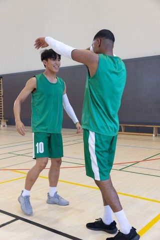 Diverse teammates celebrating high-five on indoor basketball court in green jerseys