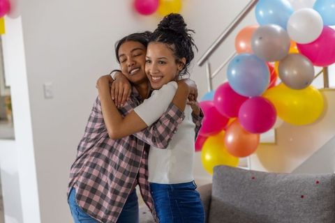 Diverse sisters hugging and smiling during colorful home celebration with balloons