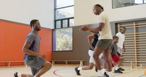 African american basketball team warming up with lunges and agility drills in gymnasium