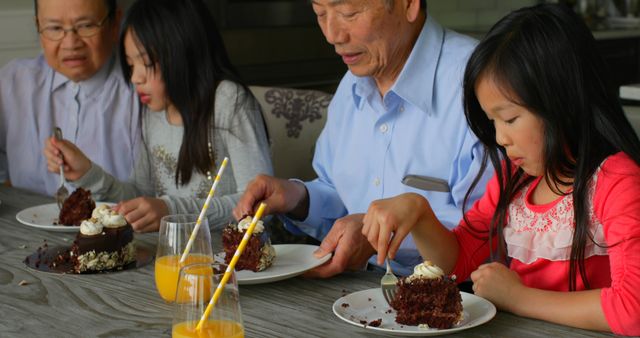 Family members of different generations are sitting together at a kitchen table, enjoying slices of chocolate cake. They drink orange juice and share pleasant moments. Perfect for illustrations of family bonding, holiday celebrations, or advertisements for family-friendly dining.