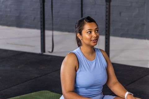 Indian fitness woman sitting on mat wearing light blue workout set and smartwatch in gym