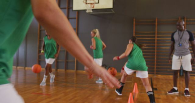 Diverse female basketball team and coach practice dribbling ball. basketball, sports training at an indoor court.