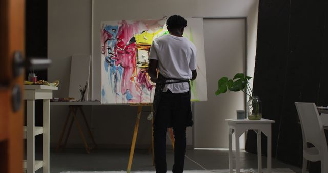 Artist standing in a modern studio, painting an abstract piece on a large canvas. Suitable for design purposes, articles on creativity and art techniques, art-related educational content, and marketing for art supplies or galleries.