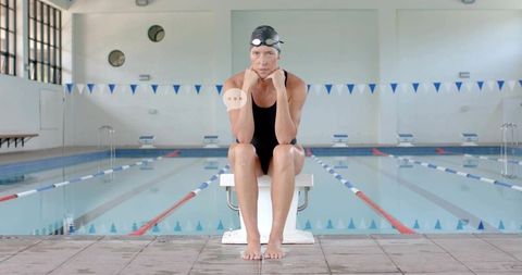 Focused Swimmer Sitting on Starting Block in Black One-Piece Swimsuit and Cap