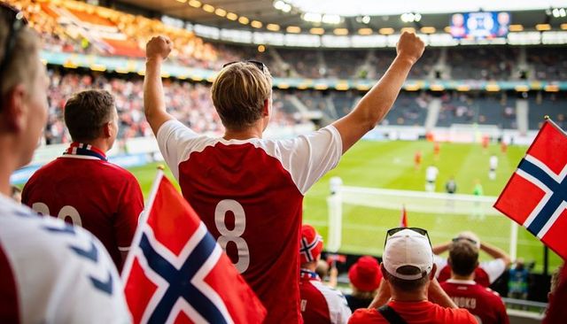 Norwegian football fans cheering in stadium raising arms and waving flags