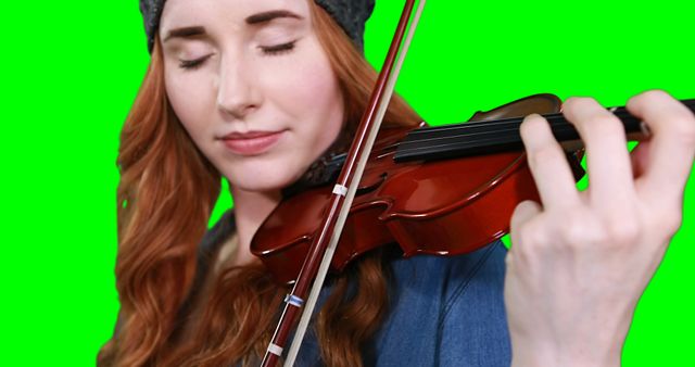 Young woman with long red hair wearing a knitted hat, playing violin with closed eyes. Perfect for ads, tutorials, and announcements related to music, performances, or artistic projects. Ideal for use in educational materials, promotional content, or background for graphic design.