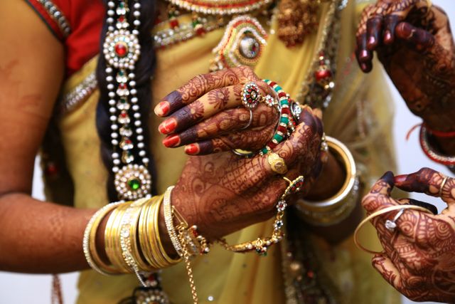 Close-up of Indian bride wearing elaborate jewelry, including bracelets and rings, and intricate henna designs on hands. Image captures the detailed artistry involved in traditional Indian weddings. Useful for content related to culture, traditions, ceremonies, or bridal fashion.
