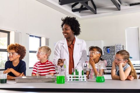Woman educator leading hands-on kids chemistry experiment with bright green solutions