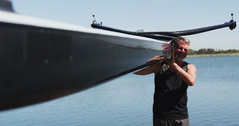 Senior Man Carrying Racing Rowing Boat by Lakeside