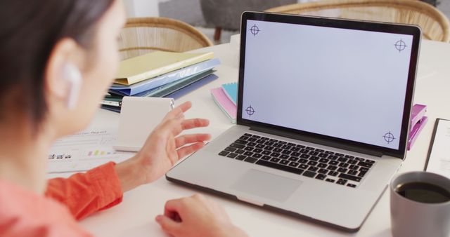 Professional setup showcasing a remote work scenario, featuring a blank laptop screen, coffee cup, and assorted office supplies on the desk. Ideal for use in articles or advertisements about virtual meetings, remote work setups, productivity tools, and digital work environments.