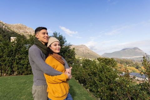 Diverse couple embracing and enjoying mountain vista on grassy terrace