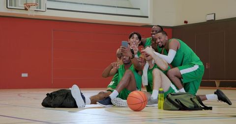 Diverse basketball teammates taking selfie on indoor court celebrating team camaraderie