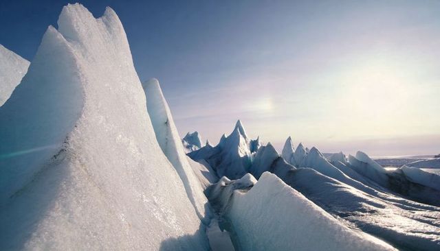 Serrated arctic ice pinnacles reflecting pale low sunlight over remote polar coastline