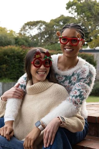 Diverse friends hugging and laughing in cozy holiday sweaters with novelty christmas glasses