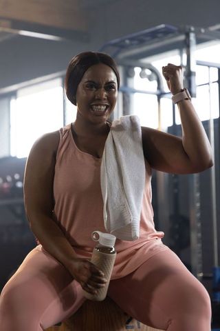 African american woman flexing bicep after workout in gym wearing pink athleticwear