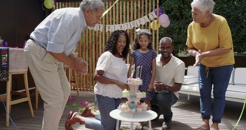 Multigenerational family celebrating child's birthday with cupcakes and candles on deck