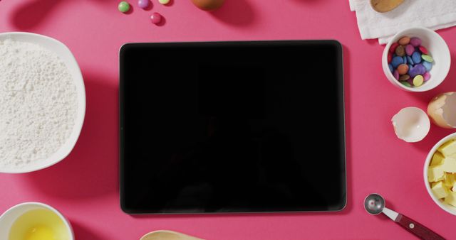 Image of baking ingredients and tools lying on pink surface with tablet with copy space. baking, food preparing, taste and flavour concept.