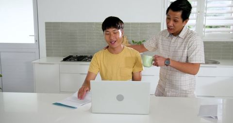 Father and teenage son engaged in discussion over laptop