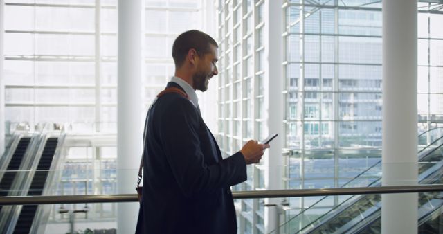 Businessman walking in contemporary office building, holding smartphone, checking messages. Suited for use in business, technology, and professional lifestyle contexts. Ideal for illustrating corporate communications, office life, or modern work environments.