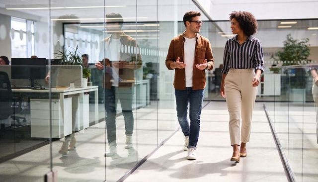 Young professionals walking and talking in glass corridor, collaborating and networking
