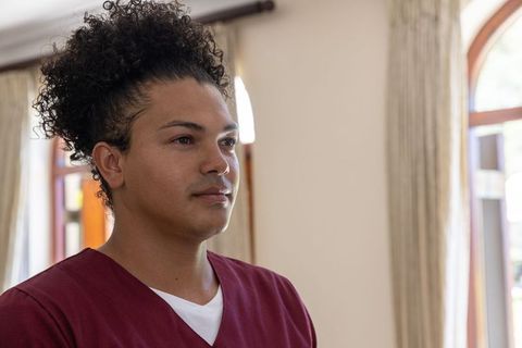 Mid-30s healthcare professional standing in maroon scrubs near arched window calm portrait