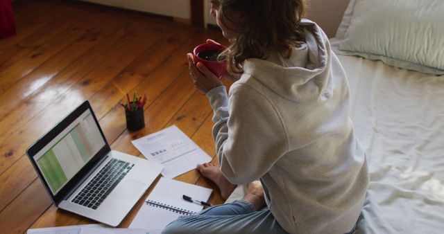 Young Woman Working from Home Holding Coffee Mug near Papers and Laptop - Download Free Stock Images Pikwizard.com