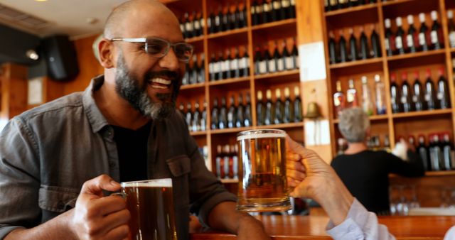 Two friends enjoying a drink at a local pub, one with a big smile. The atmosphere is warm with bottles of various beverages in the background. The scene represents relaxation, socializing, and friendship. This image can be used for themes related to nightlife, social gatherings, friendship moments, and leisure activities.