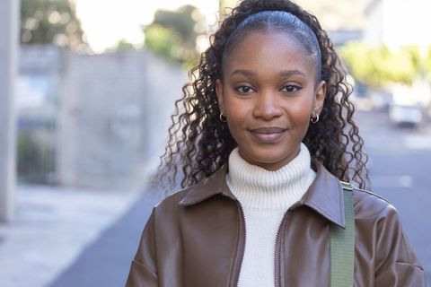 Confident african american woman standing on urban street wearing brown leather jacket