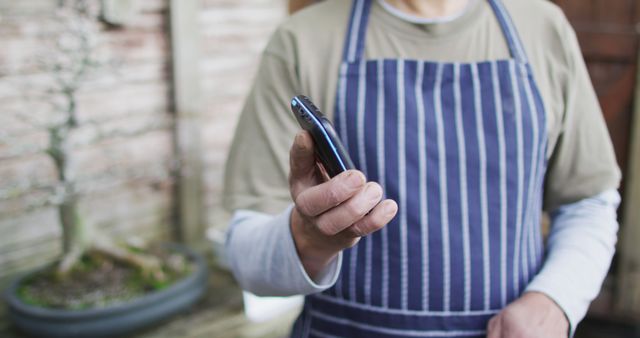 Gardener in Striped Apron Holding Smartphone in Backyard - Download Free Stock Images Pikwizard.com