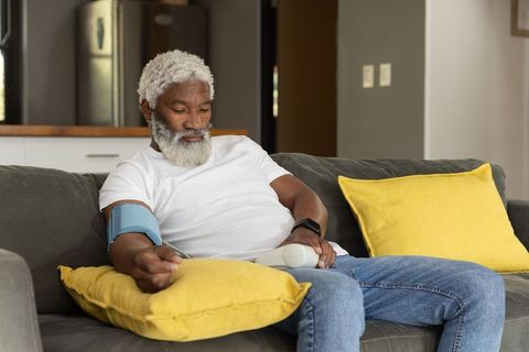 Senior african american man checking blood pressure at home on gray sofa