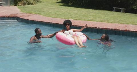 Summer pool party with african american friends enjoying donut float in backyard