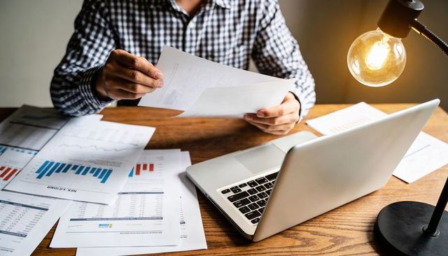 Man reviewing financial reports at laptop with desk lamp, working late on data analysis