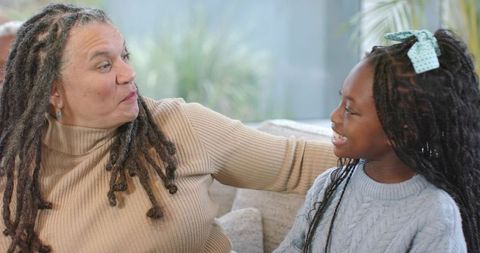 Mature Woman and African American Girl Sharing Warm Laughter and Bonding on Couch