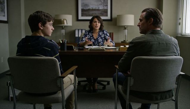 Teen and father meeting with counselor in office during family therapy consultation