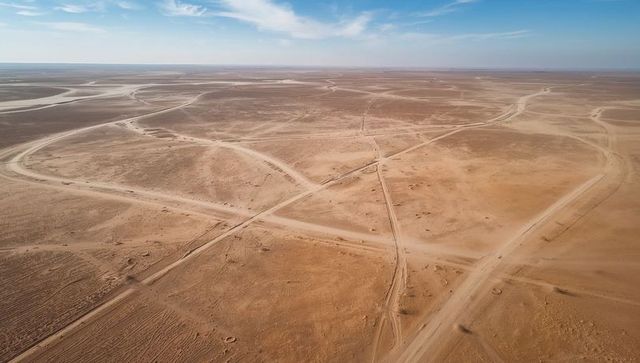 Aerial network of unpaved dirt tracks crisscrossing arid plain with crossroads and horizon