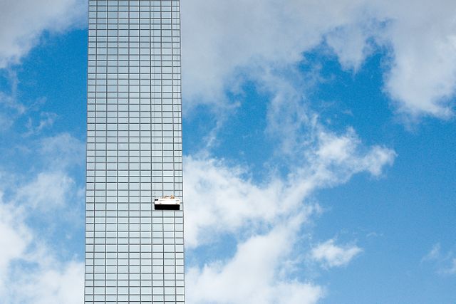 Window cleaners working on a high-rise building catching attention against blue sky backdrop. Useful for corporate presentations, safety equipment promotion, urban architecture themes, and professional cleaning service advertisements.