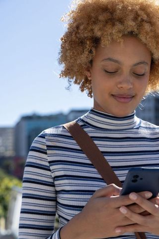 African american woman texting on smartphone in sunny urban plaza with curly hair halo
