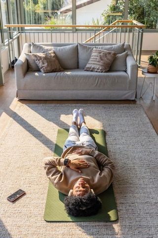 African american woman relaxing on mat in sunlit living room checking smartphone