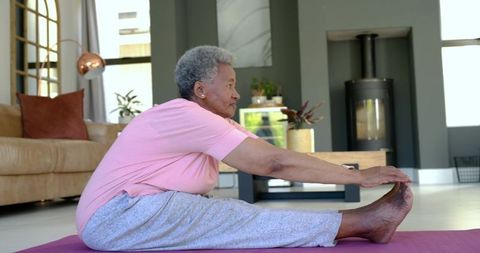 Senior african woman stretching on yoga mat at home for senior fitness and wellness