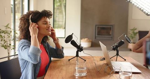 Female co-hosts putting on headphones and preparing podcast in bright home studio