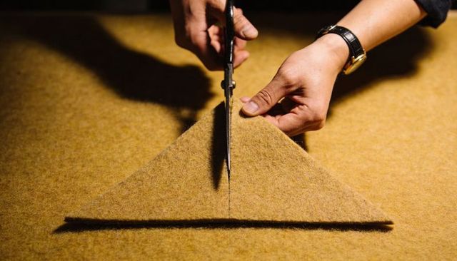Hands cutting wool felt triangle with metal shears in craft workshop closeup