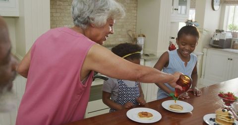 Grandmother pouring syrup while family enjoys breakfast together